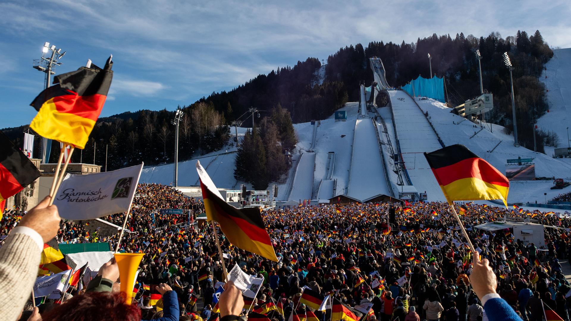 Zuschauer mit Deutschland Fahnen und Flaggen in schwarz-rot-gold im Olympia-Skisprung-Stadion Partenkirchen, dahinter Olympiaschanze im Schnee