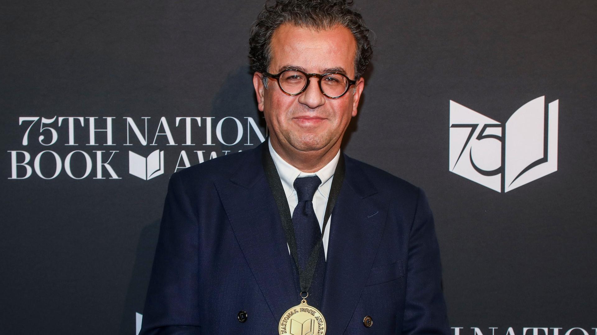 Der Autor Hisham Matar bei der Zeremonie der 75. National Book Awards im Novemeber 2024: Er steht vor einer schwarzen Wand mit dem Logo des Awards (Foto von Andy Kropa/Invision/AP) Der Autor Hisham Matar bei der Zeremonie der 75. National Book Awards im Novemeber 2024: Er steht vor einer schwarzen Wand mit dem Logo des Awards (Foto von Andy Kropa/Invision/AP)