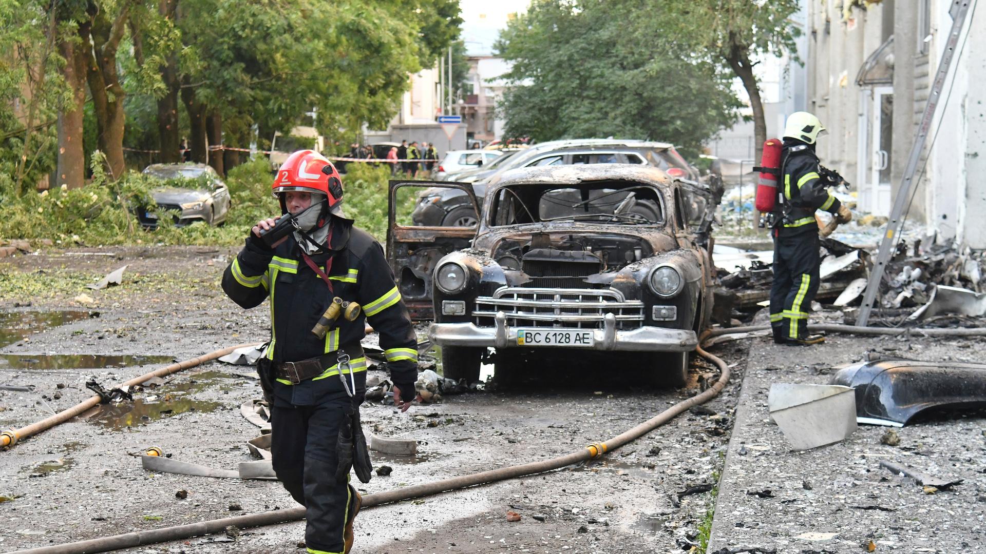 Feuerwehrleute stehen bei einem ausgebrannten Auto in der ukrainischen Stadt Lwiw.