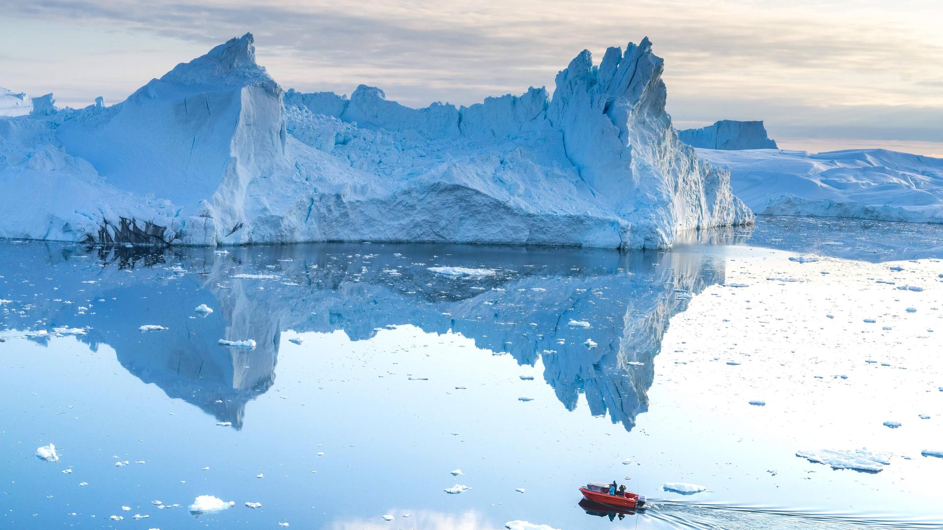 Das Bild zeigt Eisberge und ein kleines Schlauchboot, das davor im Wasser fährt.