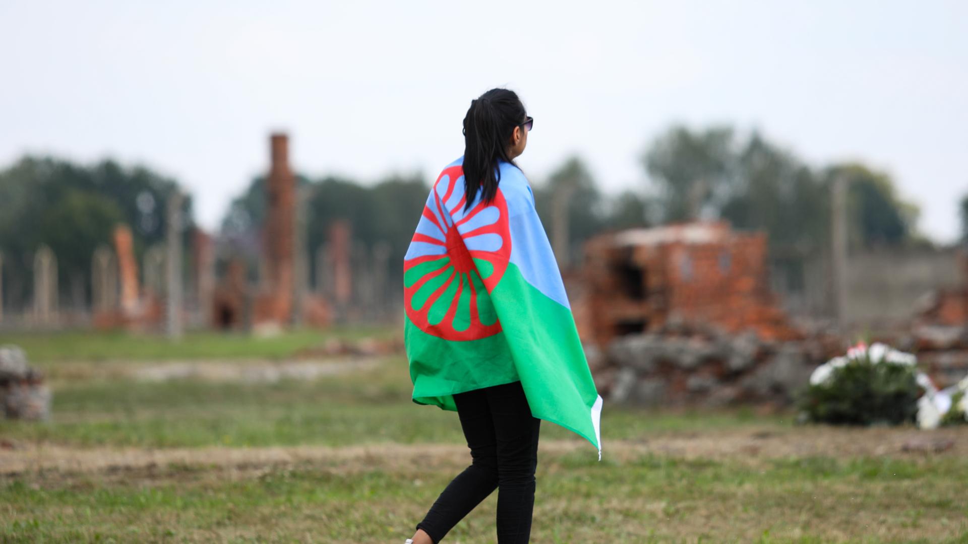 Eine junge Frau geht mit der Sinti-und-Roma-Flagge über die Gedenkstätte Auschwitz-Birkenau am 2. August 2019, dem European Roma Holocaust Memorial Day, anlässliche des 75. Jahrestags der Auflösung des sogenannten Zigeunerlagers in Auschwitz-Birkenau.
