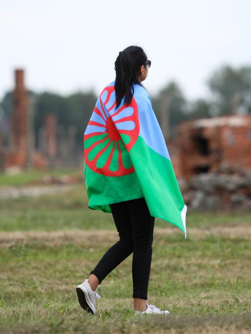 Eine junge Frau geht mit der Sinti-und-Roma-Flagge über die Gedenkstätte Auschwitz-Birkenau am 2. August 2019, dem European Roma Holocaust Memorial Day, anlässliche des 75. Jahrestags der Auflösung des sogenannten Zigeunerlagers in Auschwitz-Birkenau.