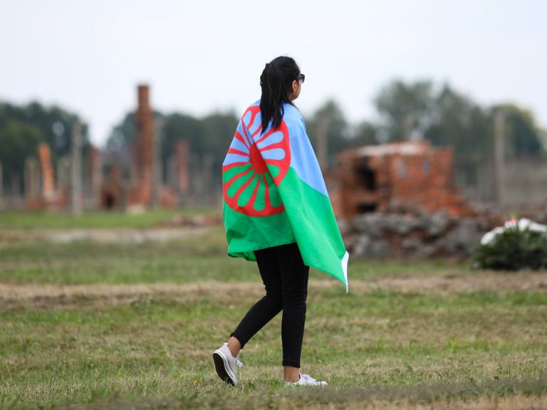 Eine junge Frau geht mit der Sinti-und-Roma-Flagge über die Gedenkstätte Auschwitz-Birkenau am 2. August 2019, dem European Roma Holocaust Memorial Day, anlässliche des 75. Jahrestags der Auflösung des sogenannten Zigeunerlagers in Auschwitz-Birkenau.