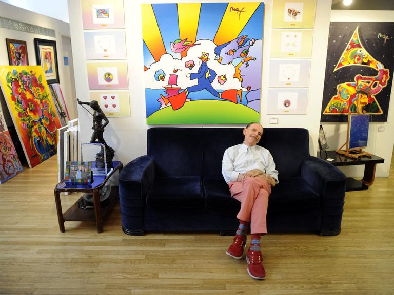 Der Pop-Art-Künstler Peter Max sitzt auf einer Couch vor einem seiner Bilder. Der Pop-Art-Künstler Peter Max sitzt auf einer Couch vor einem seiner Bilder.