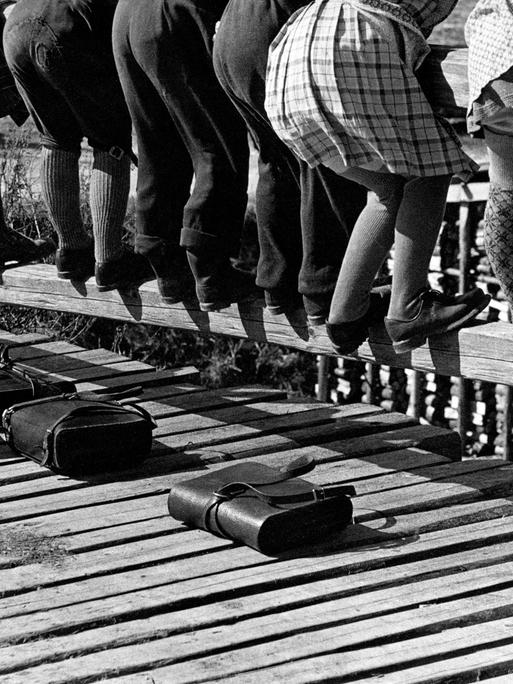 Blick auf die Beine von Schulkindern, die sich über ein Brückengeländer beugen, 1950er-Jahre.