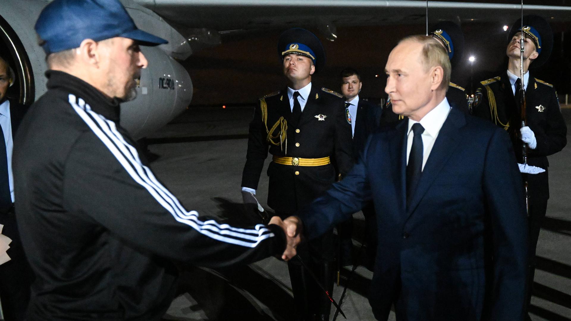 Russlands Präsident Putin schüttelt einem Mann mit blauer Kappe die Hand.