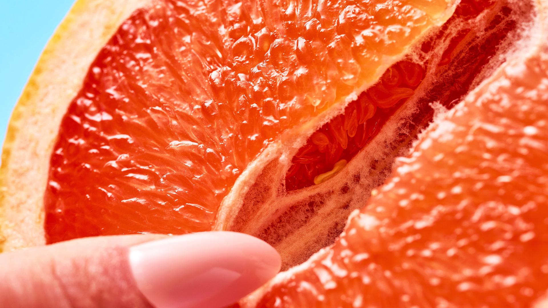 Symbolbild sexuelle Selbstbefriedigung einer Frau. Eine weibliche Hand mit langen Fingernägeln berührt zärtlich eine geöffnete Grapefruit.