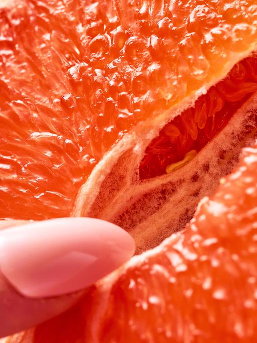 Symbolbild sexuelle Selbstbefriedigung einer Frau. Eine weibliche Hand mit langen Fingernägeln berührt zärtlich eine geöffnete Grapefruit.