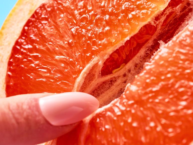 Symbolbild sexuelle Selbstbefriedigung einer Frau. Eine weibliche Hand mit langen Fingernägeln berührt zärtlich eine geöffnete Grapefruit.