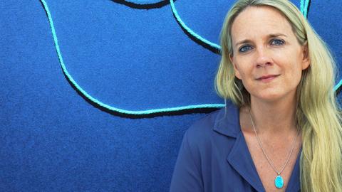 Fotografin Jessica Backhaus vor einem blauen Bild mit hellblauen Linien darin.