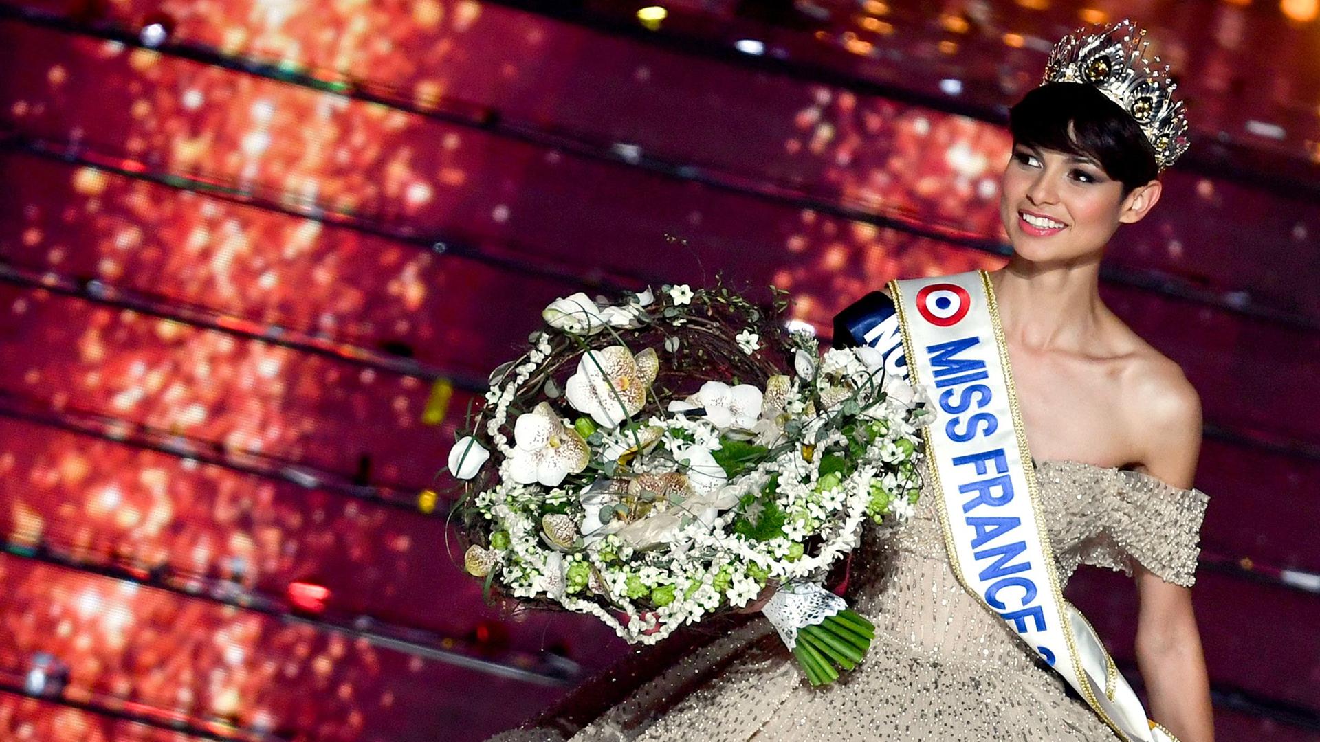 Die neugewählte Miss France 2024 mit Krone auf dem Kopf und Blumenstrauß in der Hand.