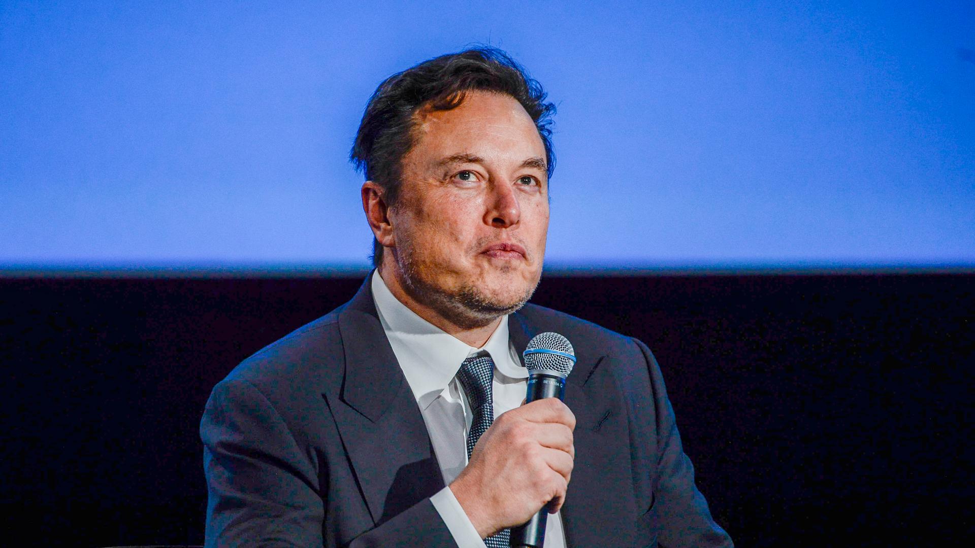 Elon Musk sitzt bei einem Interview und hält ein Mikrofon in der Hand.