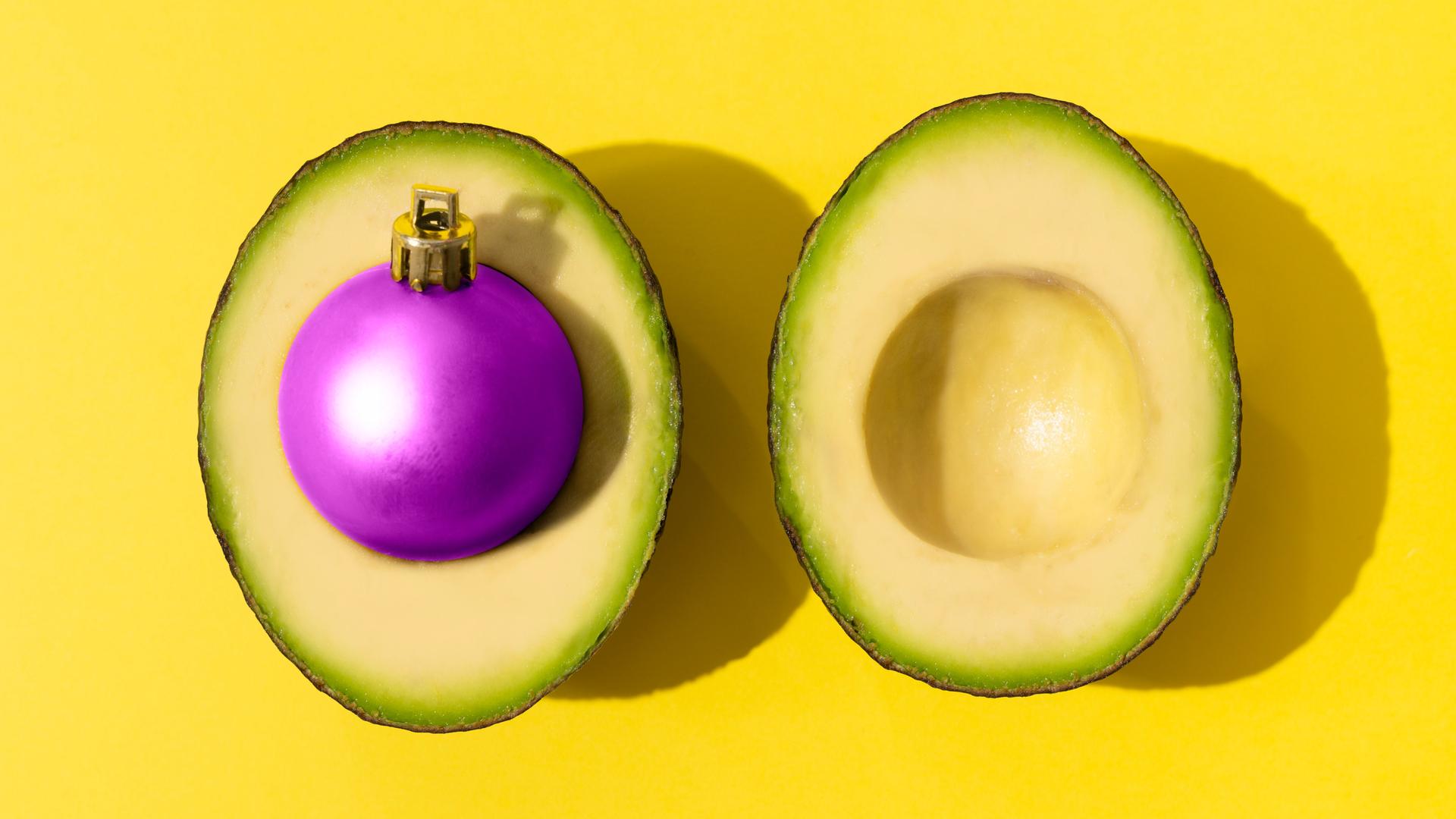 Eine Avocado mit einer violetten Weihnachtskugel als Kern.
