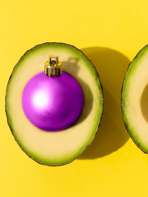 Eine Avocado mit einer violetten Weihnachtskugel als Kern.