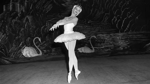 Eine Schwarz-Weiß-Fotografie der Primaballerina Maria Tallchief im New York City Ballet. Sie nimmt eine anmutige Pose ein, während sie Tschaikowsky's Schwanensee tanzt. Sie trägt Tutu und Spitzenschuhe. Im Hintergrund sind Schwäne an der Wand angemalt.