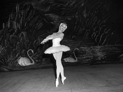 Eine Schwarz-Weiß-Fotografie der Primaballerina Maria Tallchief im New York City Ballet. Sie nimmt eine anmutige Pose ein, während sie Tschaikowsky's Schwanensee tanzt. Sie trägt Tutu und Spitzenschuhe. Im Hintergrund sind Schwäne an der Wand angemalt.