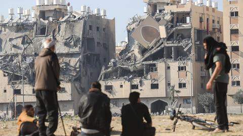 Das Foto zeigt palästinensische Zivilisten in der Stadt Chan Junis im Süden des Gazastreifens. Sie stehen vor einem zerstörten Haus.