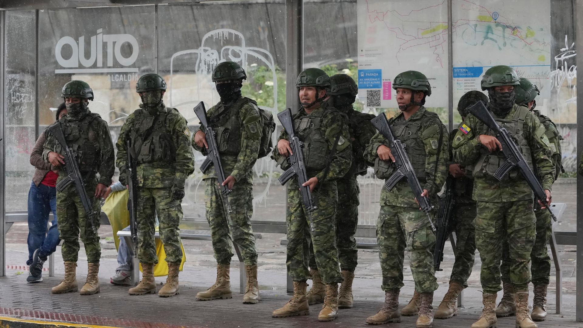 In Ecuador stehen mehrere Soldaten mit Waffen an einer Bushaltestelle.