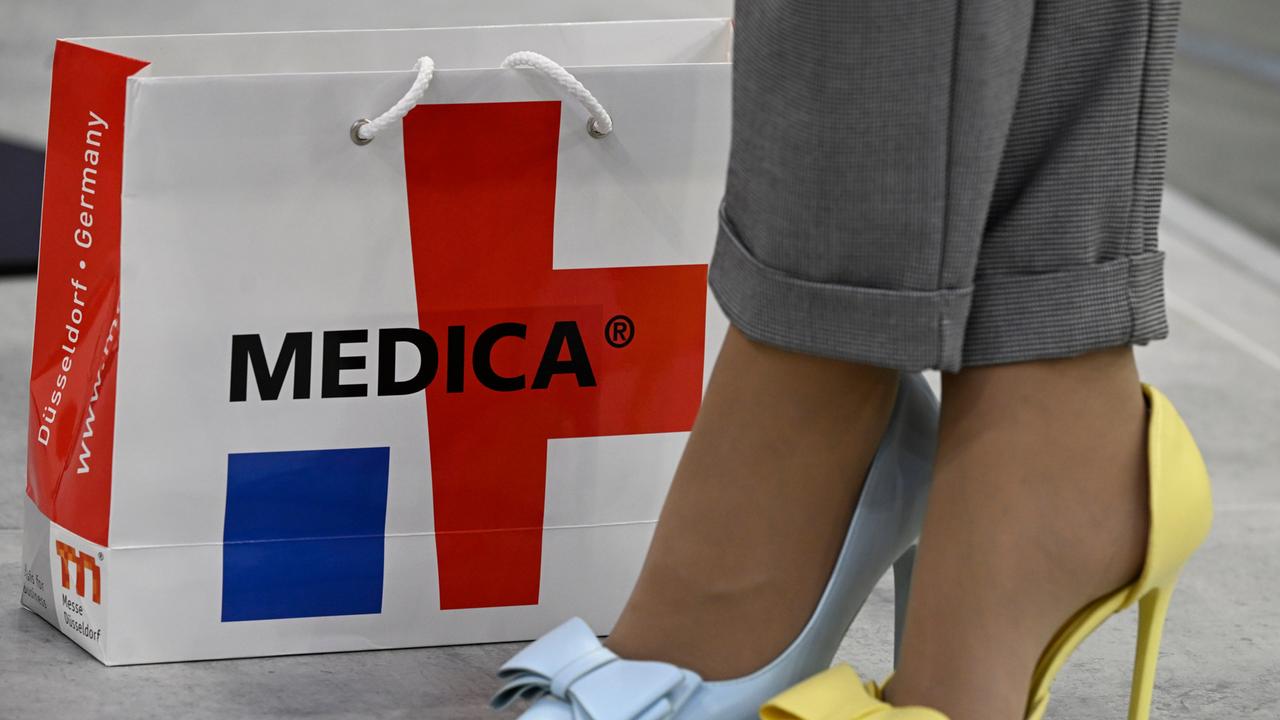 Eine Papiertüte mit der Aufschrift Medica ist auf dem Boden abgestellt. Daneben der untere Beinabschnitt einer Frau mit Pumps in zwei Farben. 