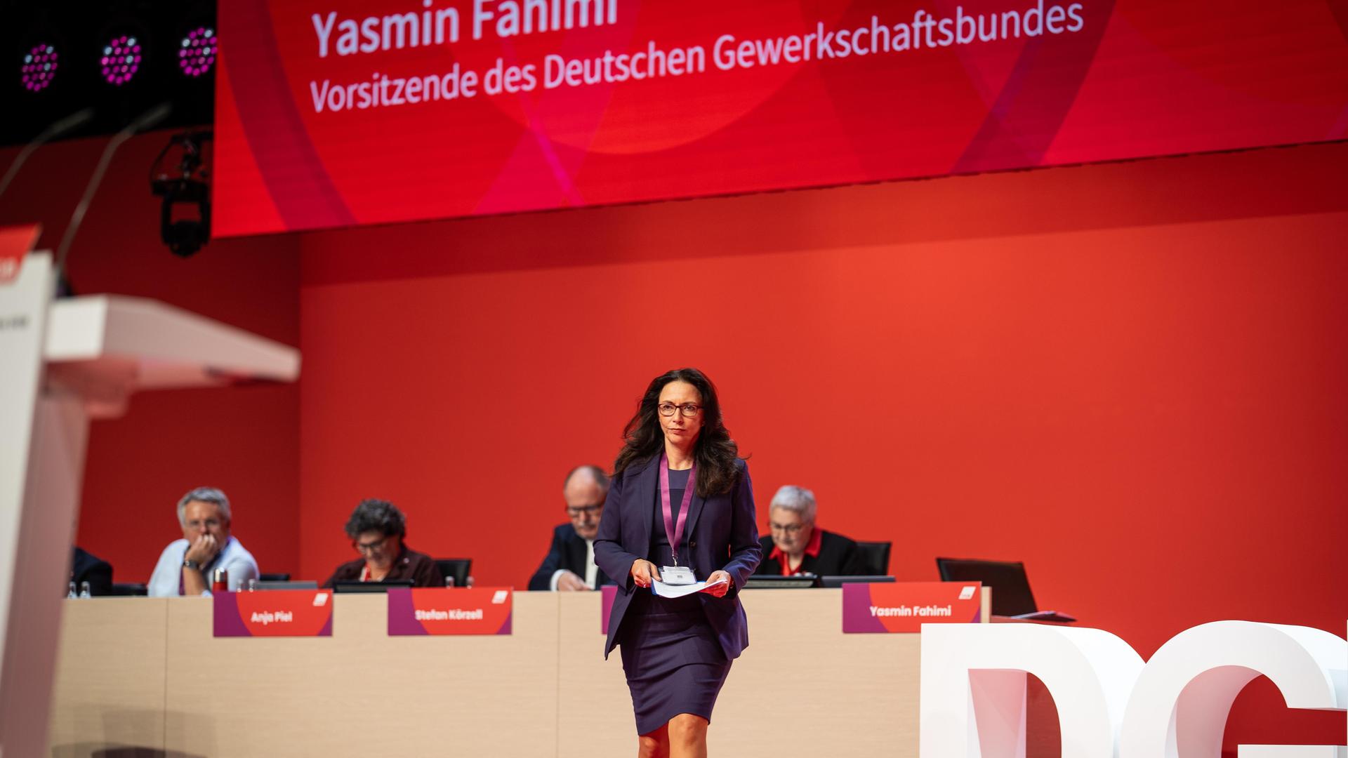 Die DGB-Vorsitzende Fahimi geht beim Bundeskongress von der Bühne; hinter ihr sitzen mehrere Personen an einem langen Tisch.