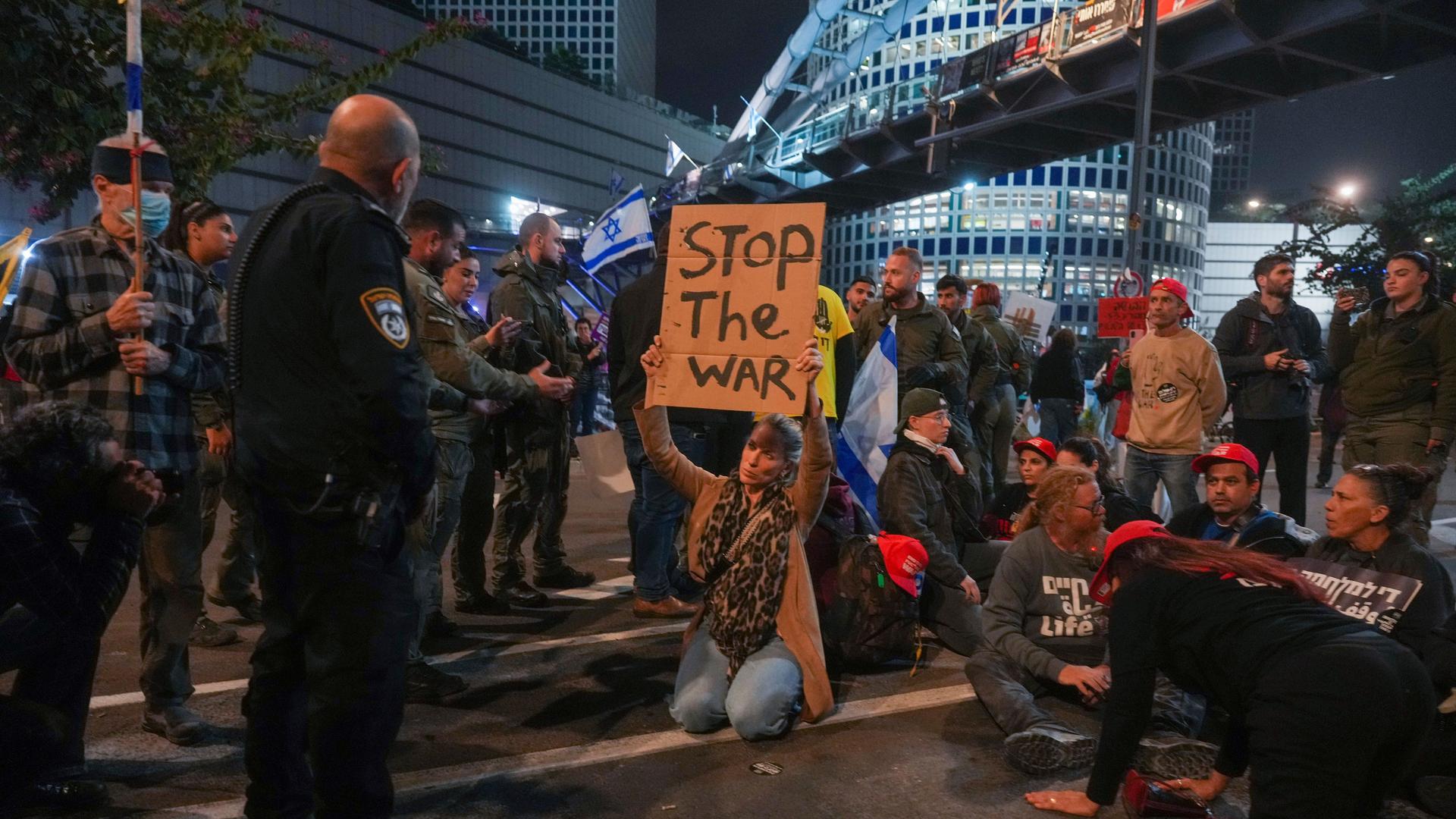 Demonstranten in Tel Aviv. Eine Frau hält ein Plakat hoch auf dem "Stop the war" - "Stoppt den Krieg" steht. Ihr steht ein Polizist gegenüber. 