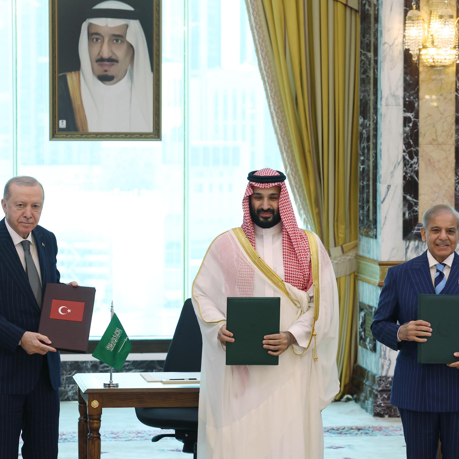 Der saudi-arabische Kronprinz bin Salman, der türkische Präsident Erdogan und der pakistanische Premierminister Sharif stehen nebeneinander und halten Dokumente in den Händen.