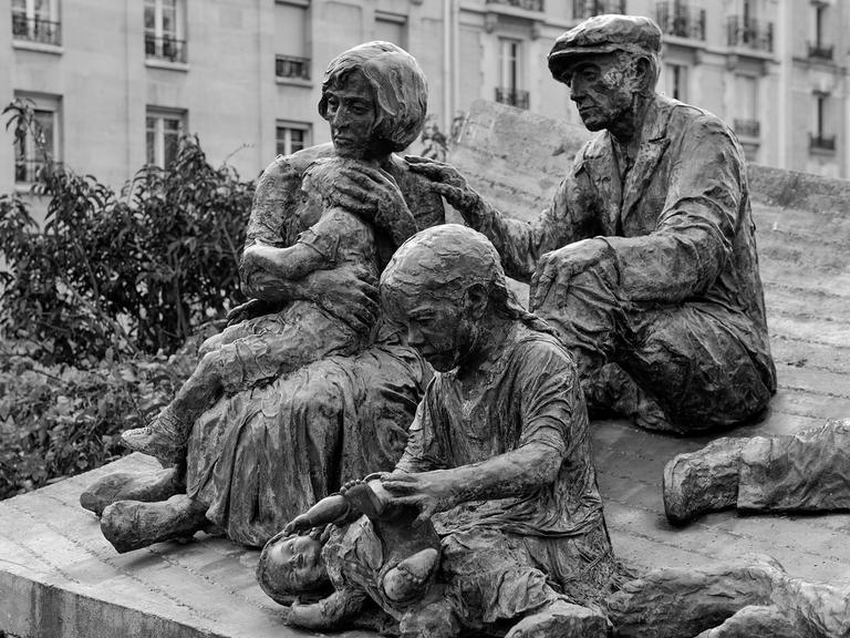 Skulptur von zwei Erwachsenen und drei Kindern, die sehr niedergeschlagen am Boden sitzen 
