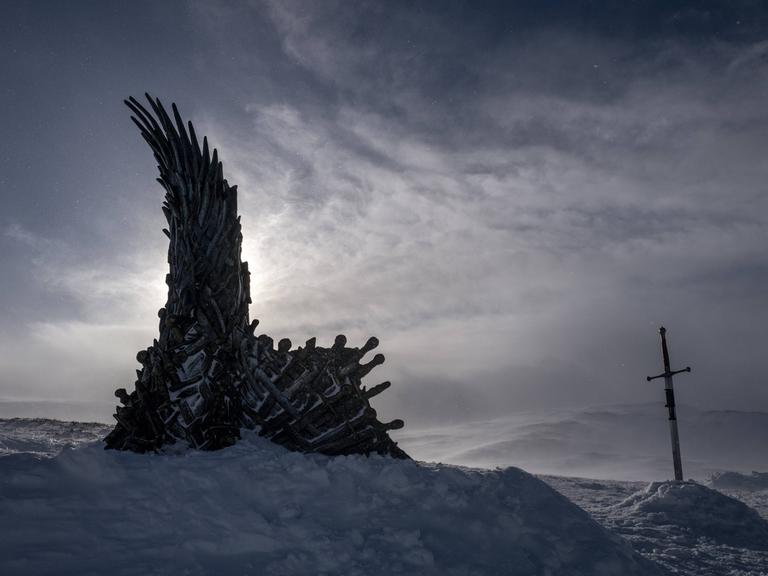 In einer düsteren Schneelandschaft steckt ein Schwert und ein Objekt was an einen metallenen Flügel erinnert.