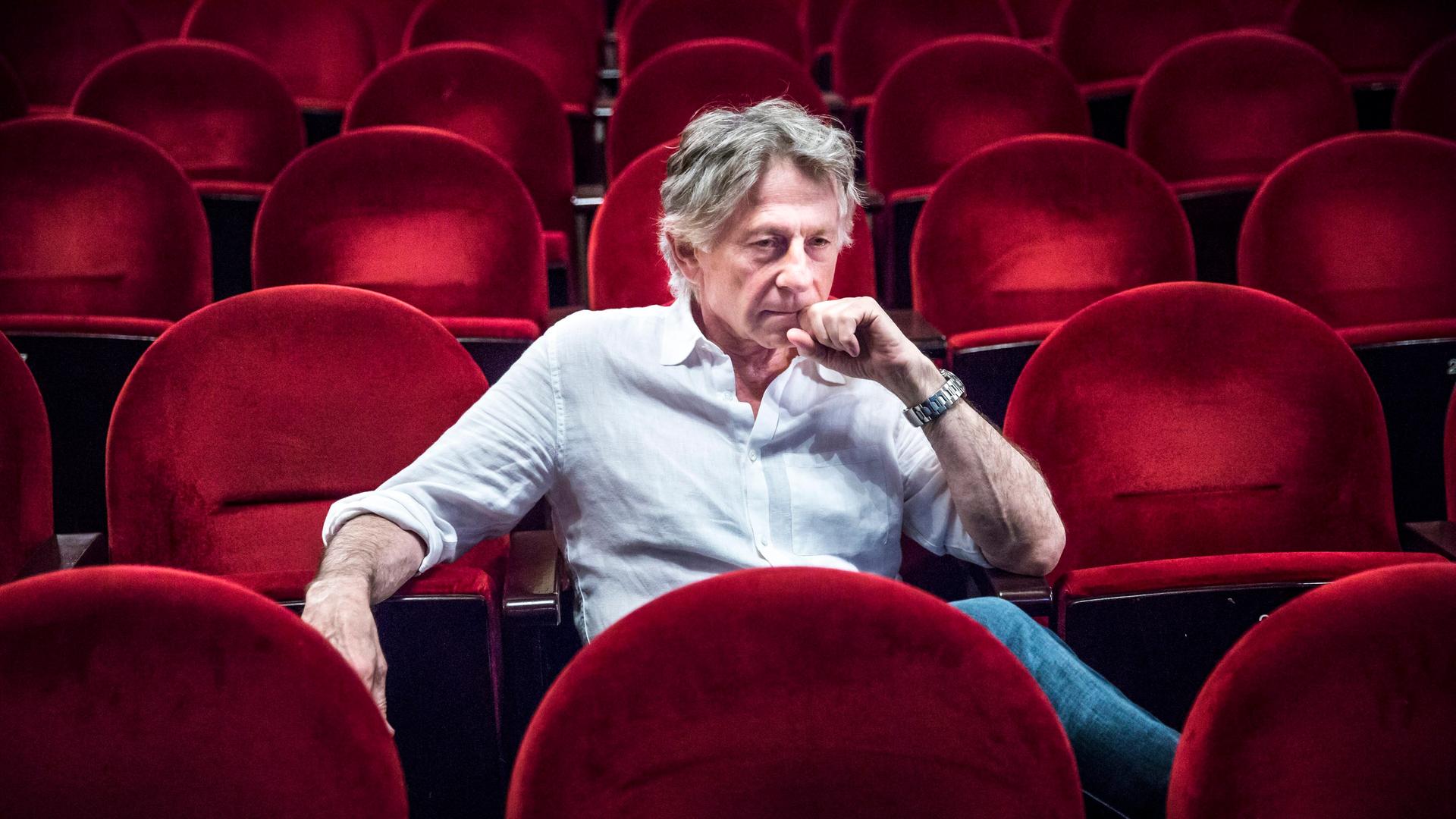 Der Filmregisseur Roman Polanski sitzt auf roten Sesseln in einem Kinosaal.
