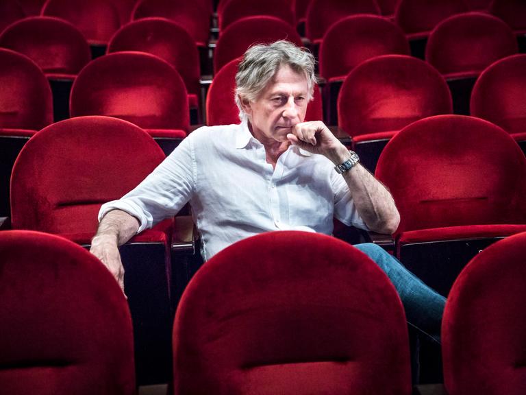 Der Filmregisseur Roman Polanski sitzt auf roten Sesseln in einem Kinosaal.