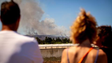 Über einer Hügellandschaft ist Rauch. Wandbrände sind am Horizont. Menschen betrachten die Feuer.