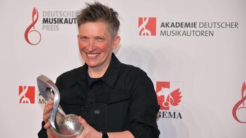 Die Kinderliedermacherin Suli Puschban steht bei einer Preisverleihung 2019 auf dem roten Teppich und hält eine Auszeichnung in der Hand.