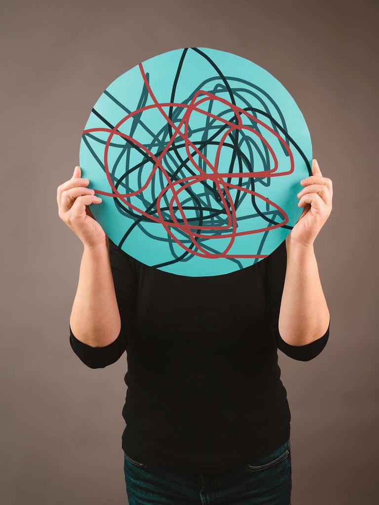 Eine Person hält sich ein rundes Schild vor das Gesicht, auf dem chaotisch verlaufende Linien zu sehen sind