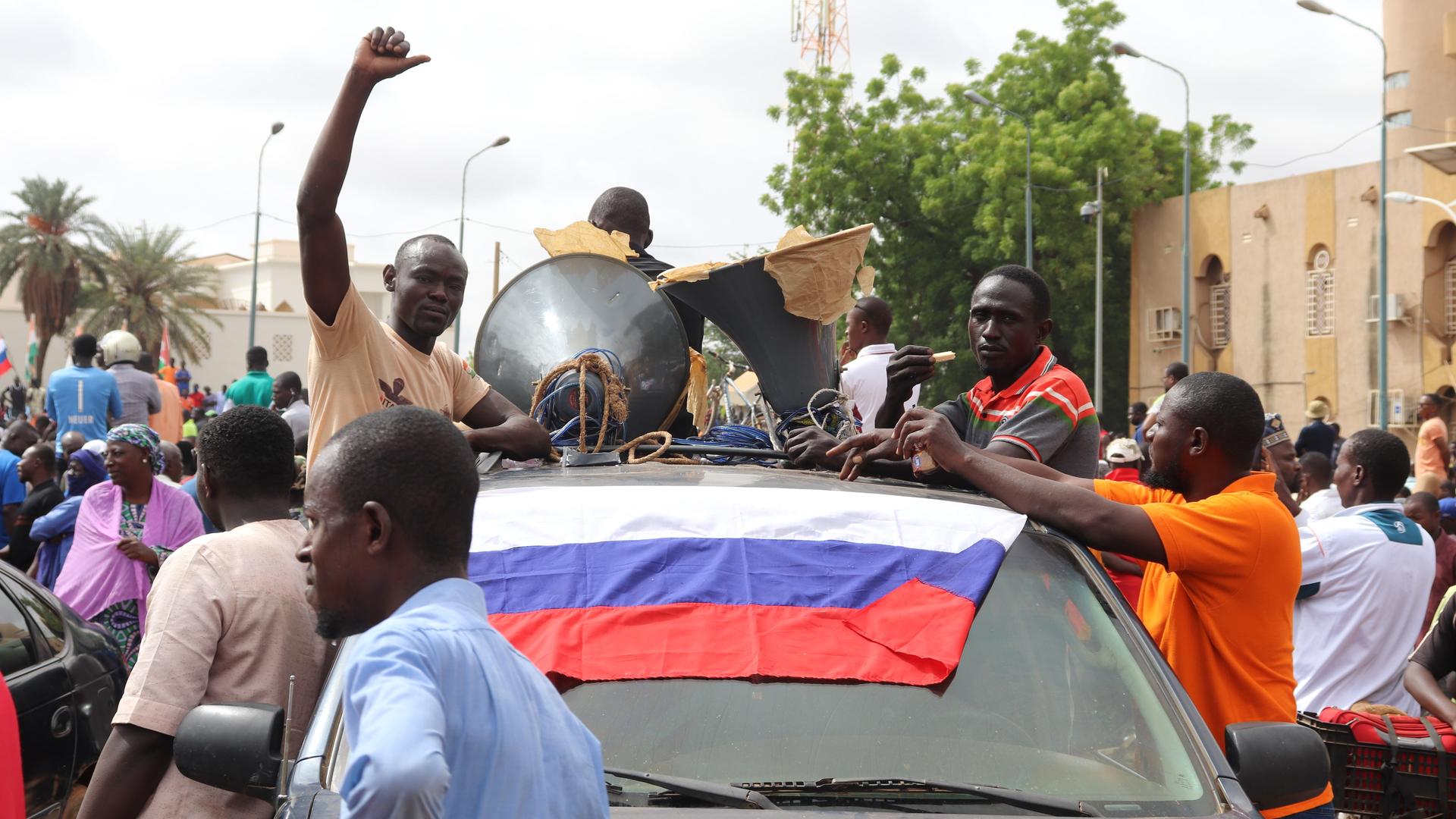 Das Foto zeigt schwarze Menschen, die in Nigers Hauptstadt Niamey demonstrieren. Auf der Windschutzscheibe eines Autos liegt eine russische Fahne in den Farben Weiß, Blau und Rot.