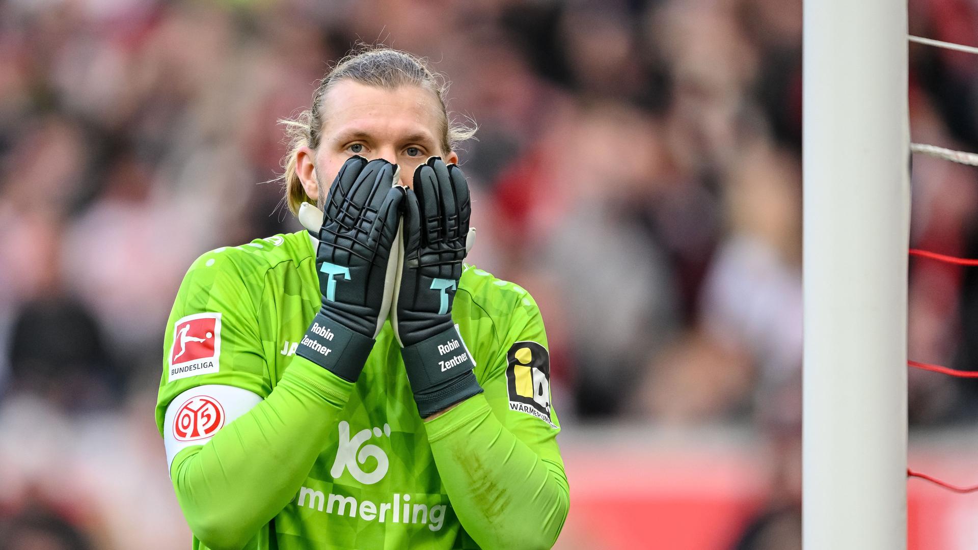 Der Mainzer Torwart Robin Zentner trägt ein grünes Trikot und schlägt die Hände vors Gesicht.
