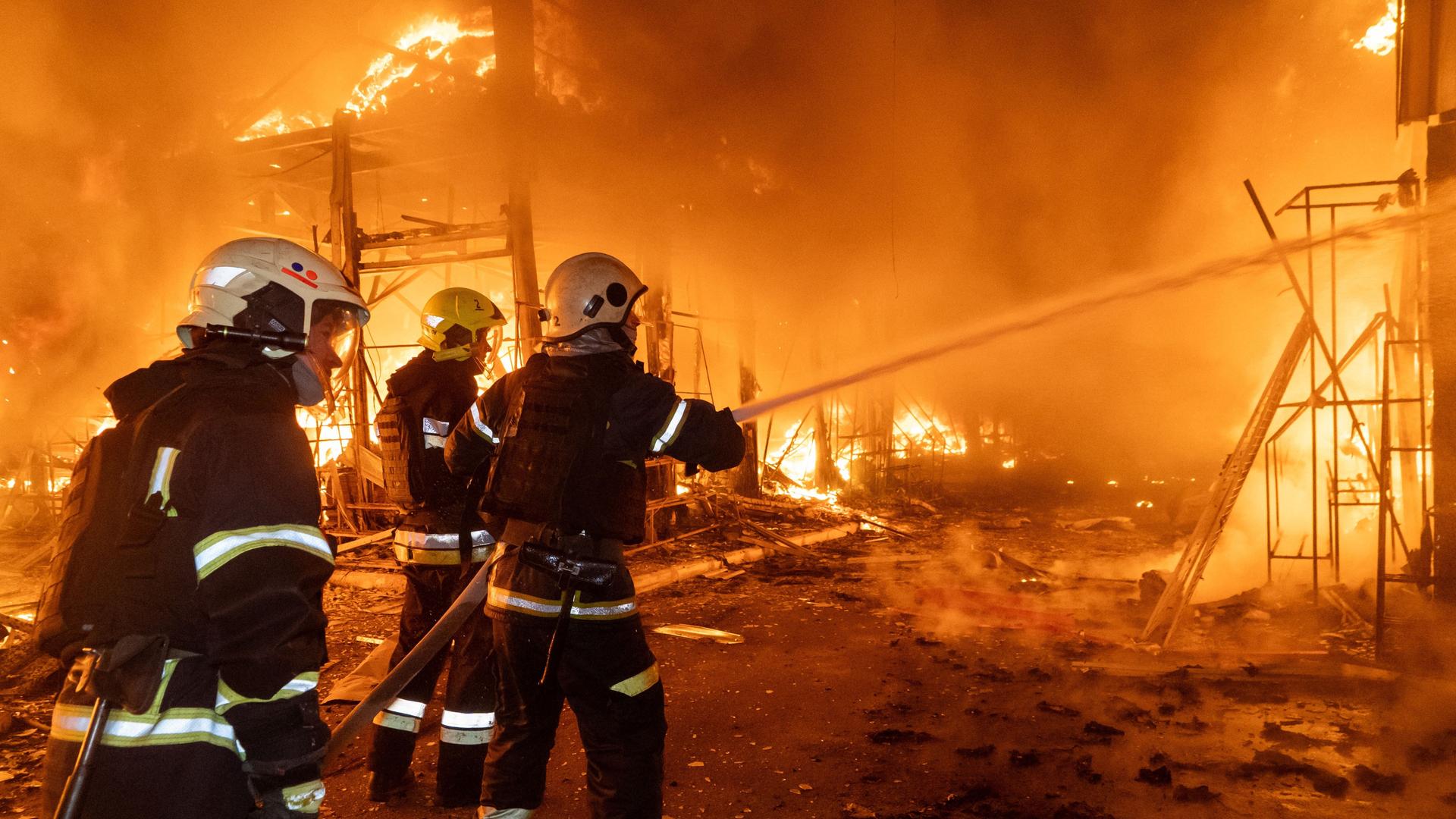 Drei Feuerwehrleute verspritzen mit einem Schlauch Wasser in die lichterloh brennende Marktruine. 