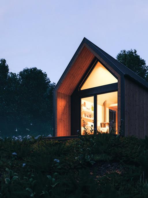 Nachtaufnahme eines von innen beleuchtenden Tiny Houses auf einer Wiese