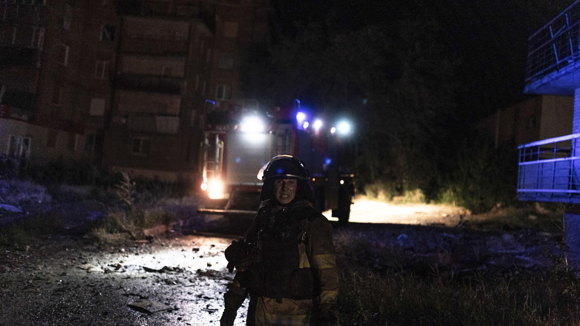 Ein Mitarbeiter der Feuerwehr steht vor einem Einsatzfahrzeug auf der Straße. Es ist dunkel. 