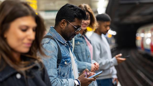 Pendler, die auf einem U-Bahnsteig warten und ihre Mobiltelefone benutzen.