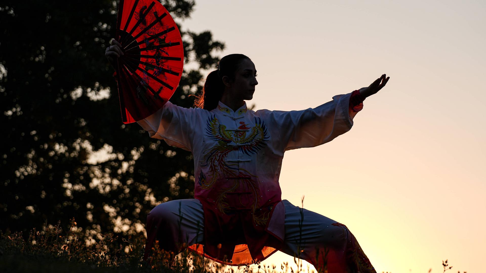 Silhouette einer Tai-Chi-Athletin mit Fächer und vor Sonnenuntergang