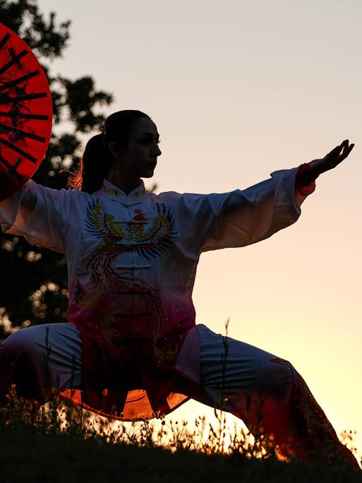 Silhouette einer Tai-Chi-Athletin mit Fächer und vor Sonnenuntergang Silhouette einer Tai-Chi-Athletin mit Fächer und vor Sonnenuntergang