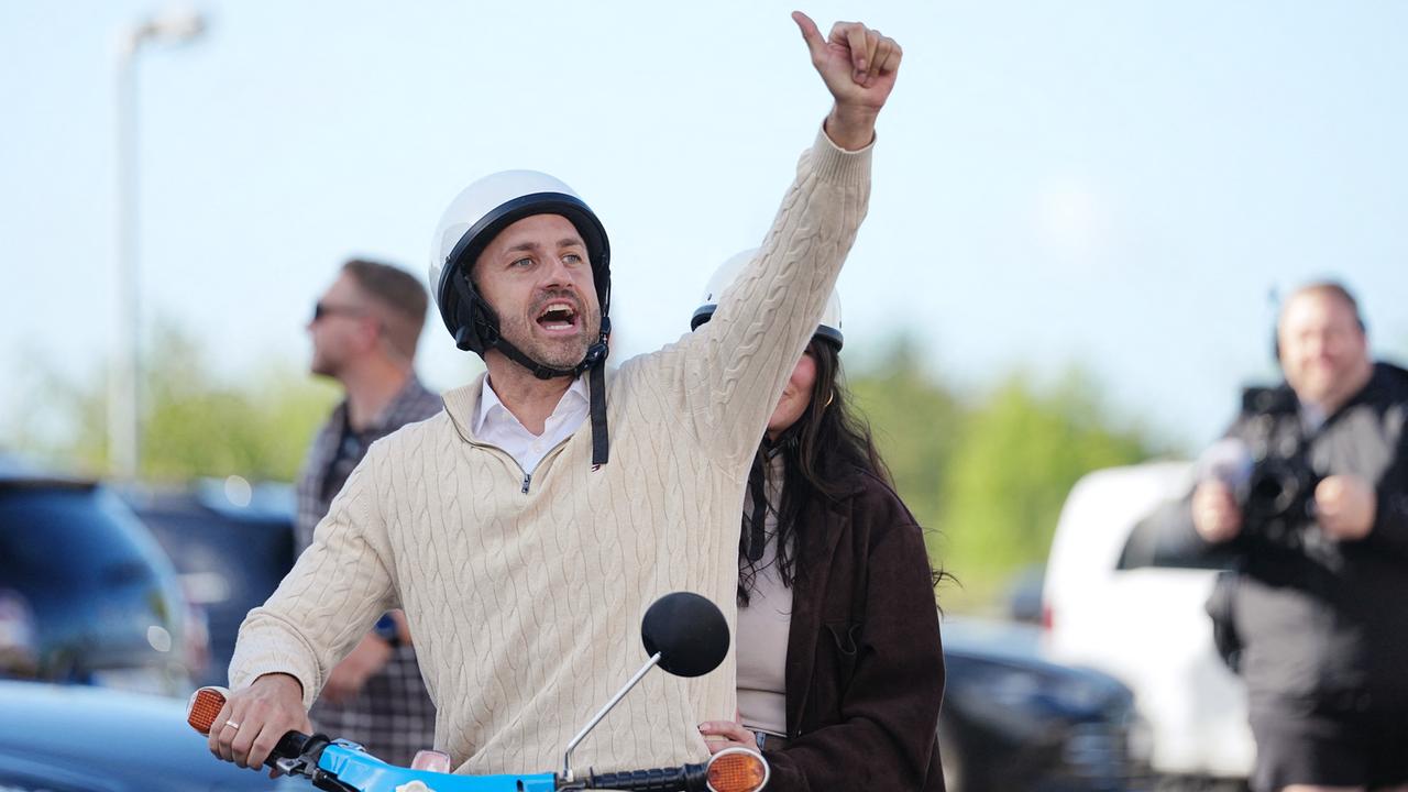 Ulrich Siegmund sitzt mit seiner Ehefrau auf einem blauen Motorroller und reckt den linken Arm in die Höhe, um "Daumen hoch" zu zeigen. 
