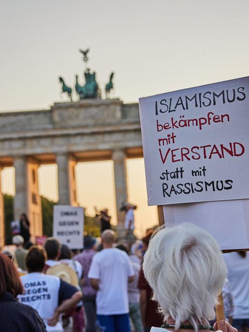 "Islamismus bekämpfen mit Verstand statt mit Rassismus" steht auf dem Plakat einer Demonstrierenden bei einer Gedenkveranstaltung für die Opfer des Attentats von Solingen vor dem Brandenburger Tor in Berlin.