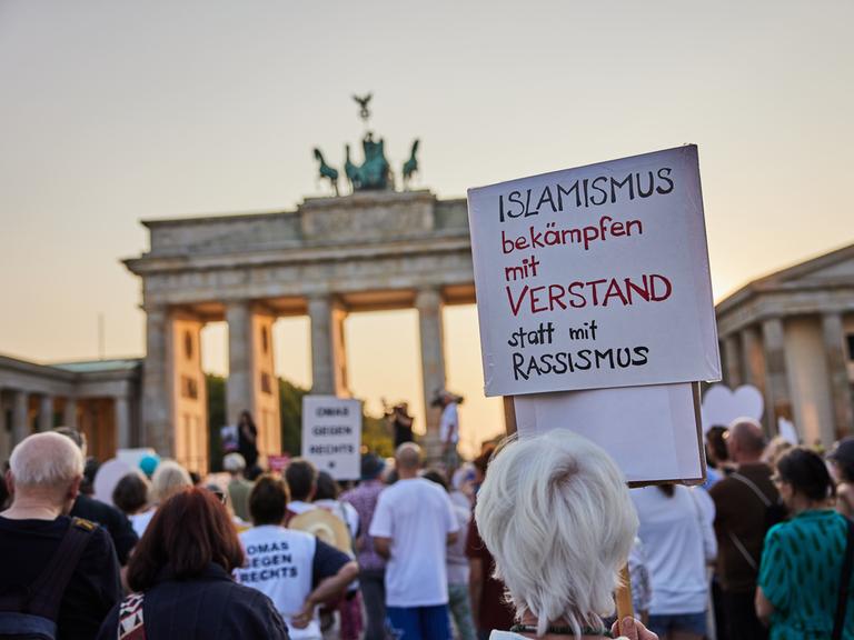 "Islamismus bekämpfen mit Verstand statt mit Rassismus" steht auf dem Plakat einer Demonstrierenden bei einer Gedenkveranstaltung für die Opfer des Attentats von Solingen vor dem Brandenburger Tor in Berlin.