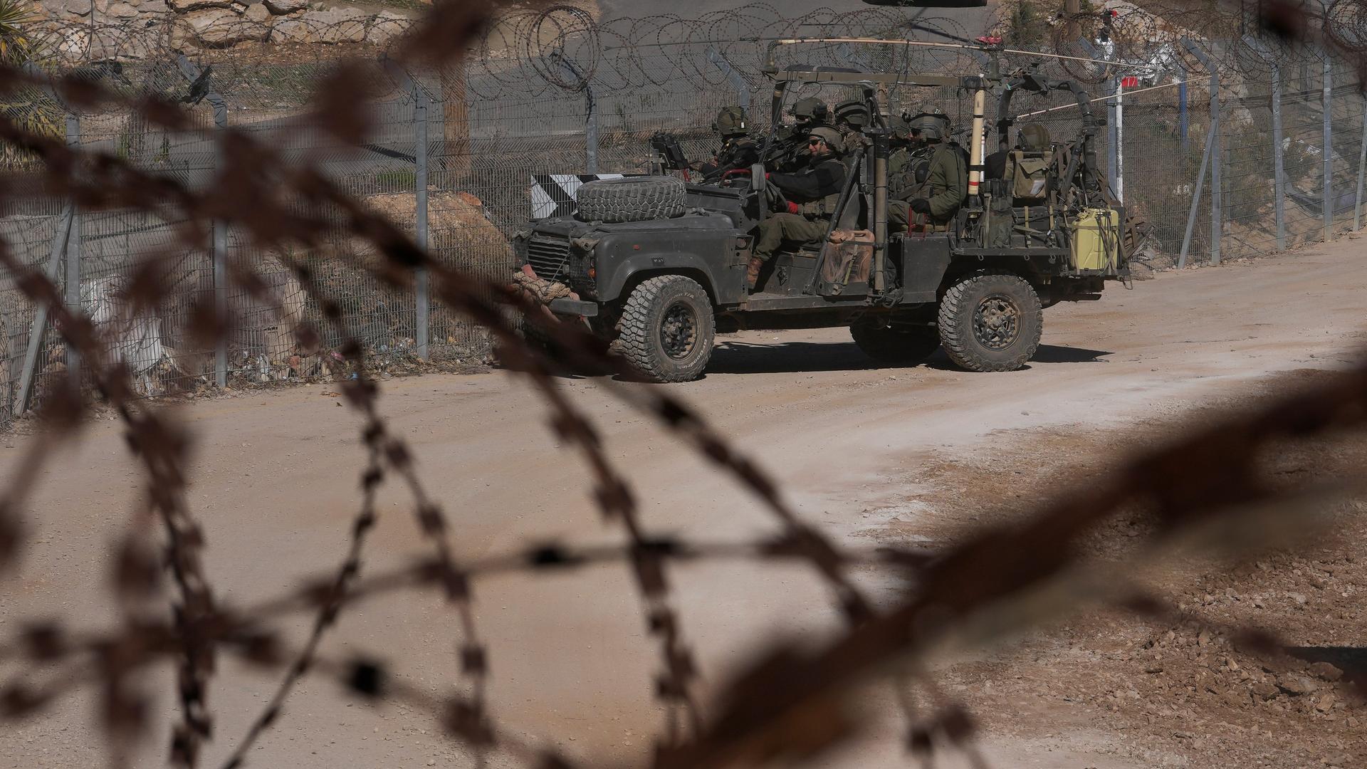 Israelische Soldaten stehen vor einem Zaun mit Stacheldraht auf einem gepanzerten Fahrzeug. 