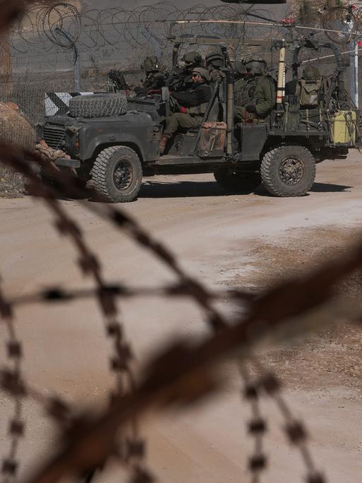 Israelische Soldaten stehen vor einem Zaun mit Stacheldraht auf einem gepanzerten Fahrzeug. 