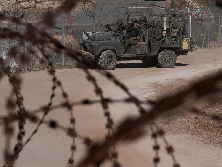 Israelische Soldaten stehen vor einem Zaun mit Stacheldraht auf einem gepanzerten Fahrzeug. 