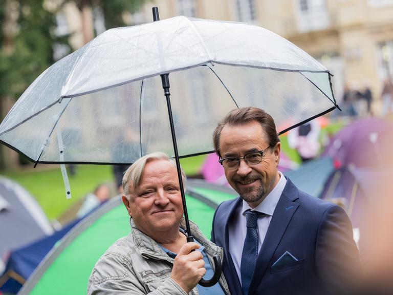 Axel Prahl (Hauptkommissar Frank Thiel, l), Schauspieler, und Jan Josef Liefers (Prof. Dr. Karl-Friedrich Boerne), Schauspieler, stehen am Set vom Münster «Tatort» zwischen Zelten im Park hinter dem Schloss. Die neue Episode «Ich gestehe» (AT) thematisiert Wohnungsnot unter Studierenden.