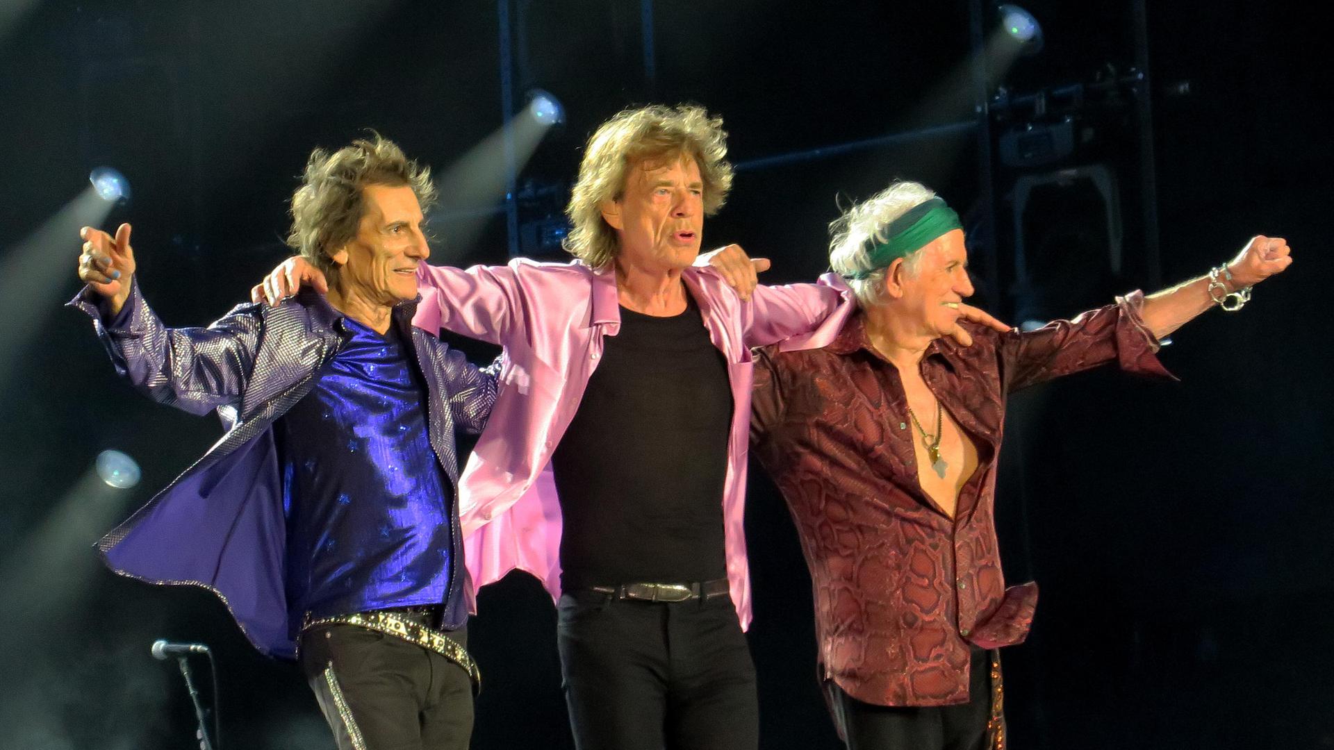 Die "Rolling Stones" auf der Bühne. Ron Wood, Mick Jagger und Keith Richards stehen nebeneinander und haben die Arme auf ihre Schultern gelegt. Die "Rolling Stones" auf der Bühne. Ron Wood, Mick Jagger und Keith Richards stehen nebeneinander und haben die Arme auf ihre Schultern gelegt.