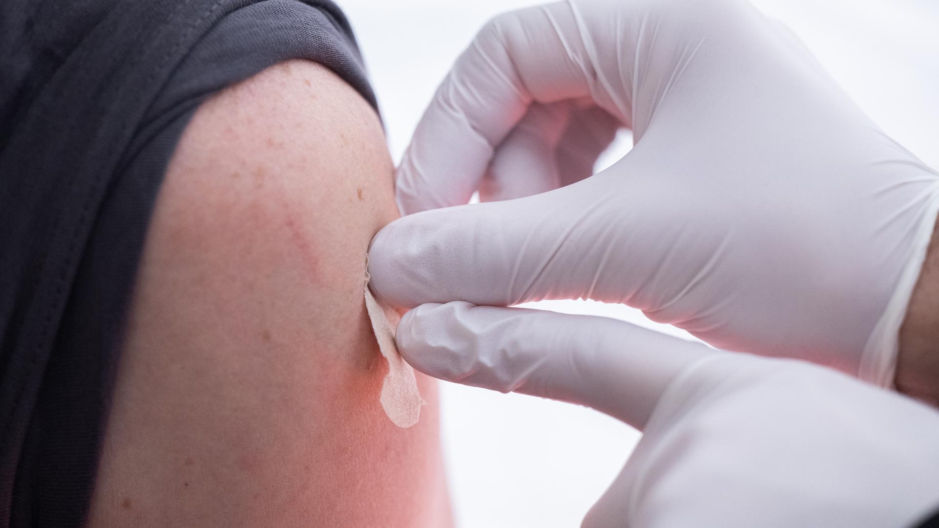 Eine geimpfte Person bekommt vom Arzt ein Pflaster auf die Nadeleinstichstelle am Oberarm.
